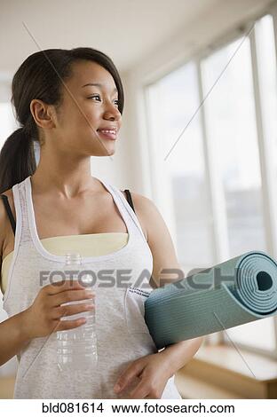 Picture - Smiling mixed race teenage girl holding yoga mat and water bottle. Fotosearch