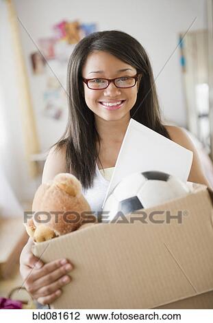 Stock Image - Smiling mixed race teenage girl holding box of belongings. Fotosearch