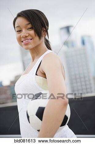 Stock Image - Smiling mixed race teenage girl holding soccer ball. Fotosearch