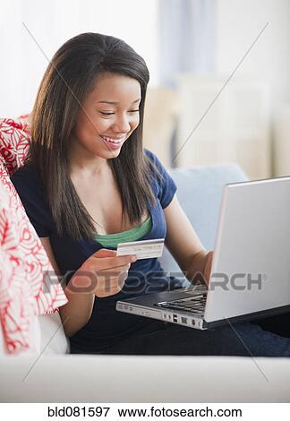 Smiling mixed race teenage girl holding credit card and laptop on sofa View Large Photo Image Stock Photo - Smiling mixed race teenage girl holding credit card and laptop on sofa. Fotosearch