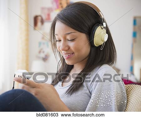 Stock Image - Smiling mixed race teenage girl listening to headphones. Fotosearch