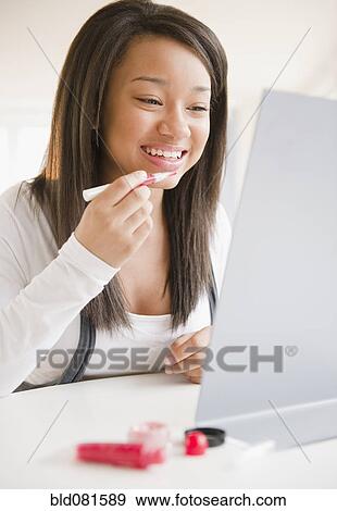 Smiling mixed race teenage girl applying lip gloss in mirror View Large Photo Image Stock Photo - Smiling mixed race teenage girl applying lip gloss in mirror. Fotosearch