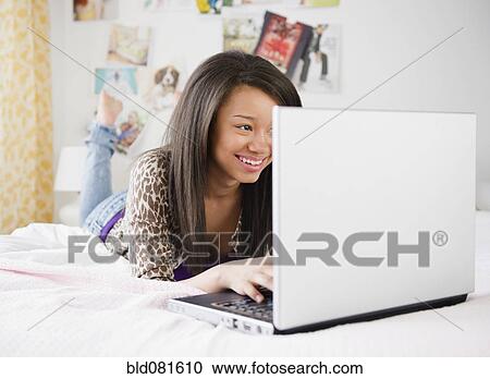 Smiling mixed race teenage girl using laptop on bed View Large Photo Image Stock Image - Smiling mixed race teenage girl using laptop on bed. Fotosearch