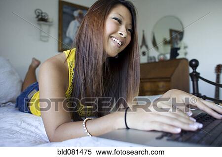 Stock Photography - Smiling mixed race teenage girl using laptop on bed. Fotosearch