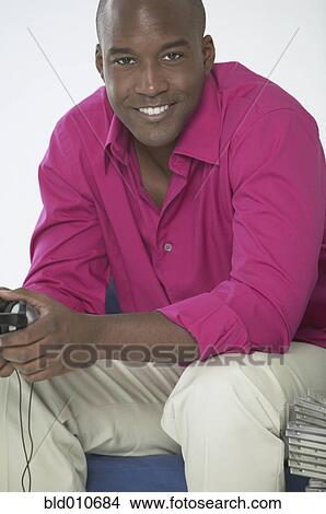 Picture - African American man sitting and holding headphones. Fotosearch