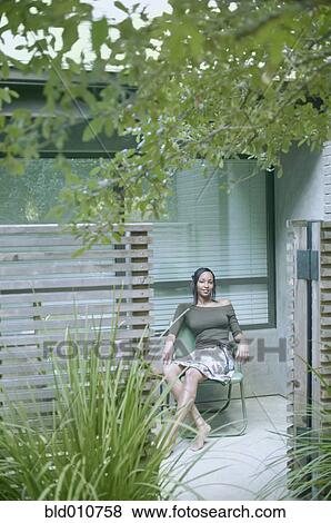 Stock Photo - African American woman sitting in chair next to house. Fotosearch