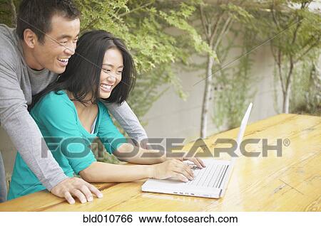 Stock Photograph - Asian couple using laptop outdoors. Fotosearch