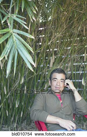 Asian man sitting in chair under bamboo View Large Photo Image Picture - Asian man sitting in chair under bamboo. Fotosearch