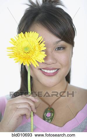 Stock Image - Asian woman holding flower in front of one eye. Fotosearch