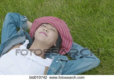 Stock Image - Asian woman laying in grass with eyes closed. Fotosearch