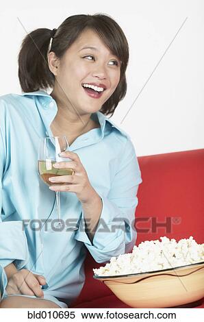 Stock Photography - Asian woman wearing man's shirt on sofa with wine. Fotosearch