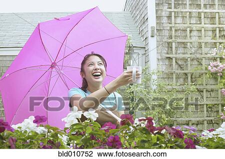 Stock Image - Asian woman with umbrella holding mug out in rain. Fotosearch