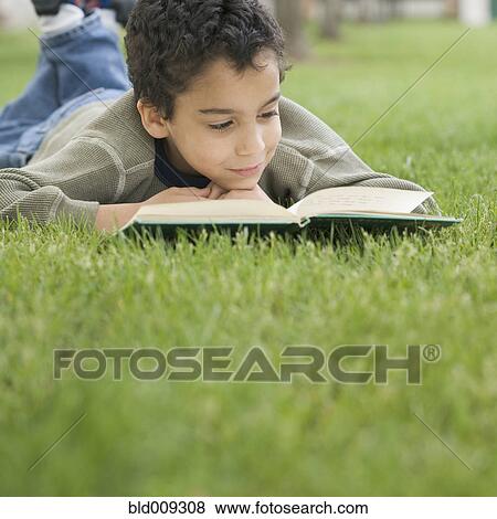 Stock Photo - Boy reading book while lying on lawn. Fotosearch
