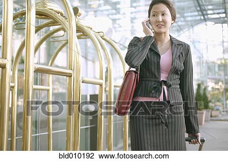 Stock Image - Businesswoman on mobile phone in hotel lobby. Fotosearch