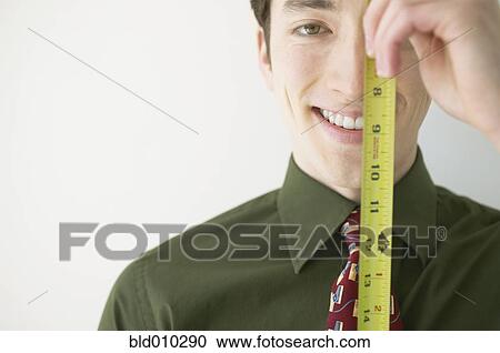 Stock Image - Close-up of a businessman holding a ruler in front of his face. Fotosearch