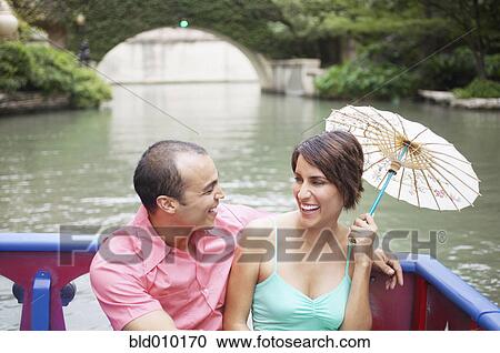Stock Image - Couple sitting in a boat with parasol. Fotosearch