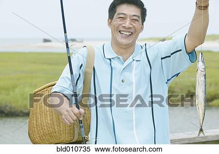Stock Photography - Middle-aged Asian man holding up fishing pole and fish. Fotosearch
