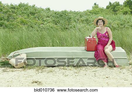 Middle-aged Asian woman sitting on upside down boat on beach View Large Photo Image Stock Photograph - Middle-aged Asian woman sitting on upside down boat on beach . Fotosearch