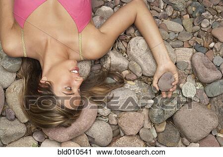 Stock Image - Portrait of young woman lying on rocks. Fotosearch