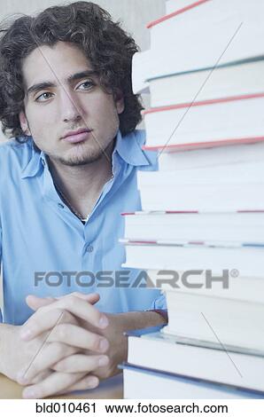 Stock Image - Teenage boy looking at stack of books. Fotosearch