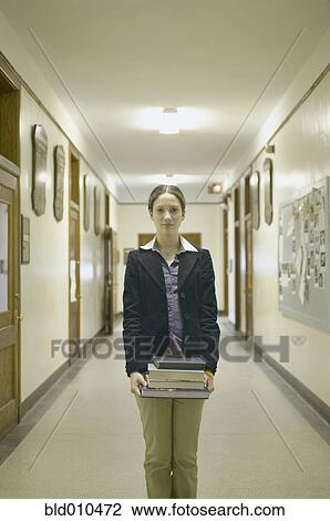 Stock Image - Teenage girl holding books in corridor. Fotosearch