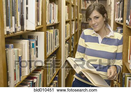 Stock Image - Teenage girl standing in library aisle. Fotosearch