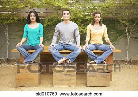 Three friends sitting on table with feet on benches outdoors View Large Photo Image Stock Photo - Three friends sitting on table with feet on benches outdoors. Fotosearch