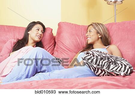Stock Image - Two women sitting together on bed. Fotosearch