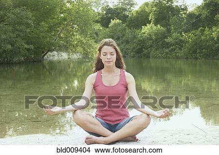 Picture - Woman in lotus position beside water. Fotosearch