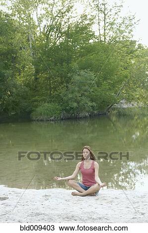 Woman in lotus position beside water View Large Photo Image Stock Image - Woman in lotus position beside water. Fotosearch
