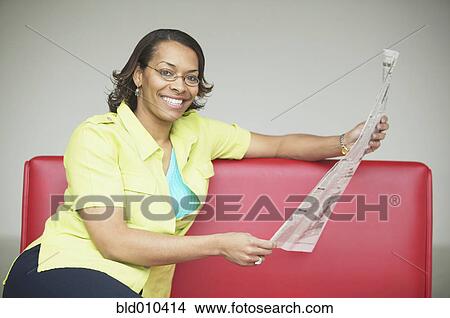 Picture - Woman on couch with newspaper. Fotosearch