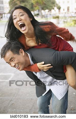 Stock Image - Woman riding piggyback on a young man. Fotosearch