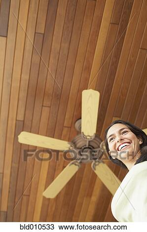 Stock Image - Woman standing under ceiling fan. Fotosearch