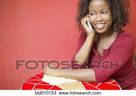 Stock Image - Woman using mobile phone at outdoor table. Fotosearch