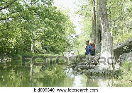 Stock Image - Young man hiking alongside water. Fotosearch