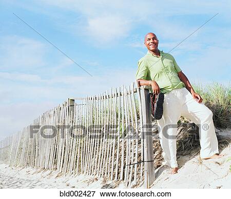 Stock Photo - Young man leaning on beach fence. Fotosearch