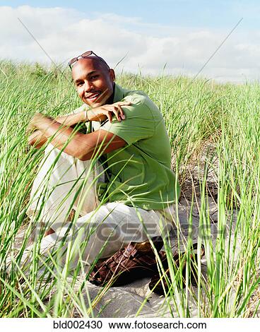 Young man sitting in sea grass on beach View Large Photo Image Stock Image - Young man sitting in sea grass on beach. Fotosearch