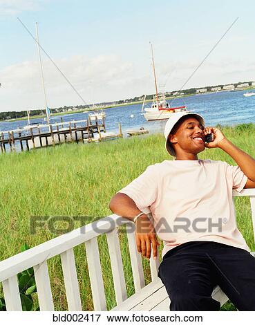 Stock Photo - Young man using cell phone at waterfront. Fotosearch