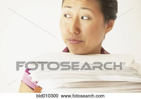 Stock Image - Young woman carrying a stack of papers. Fotosearch