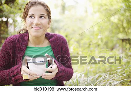 Young woman holding a cup in garden View Large Photo Image Stock Photo - Young woman holding a cup in garden. Fotosearch