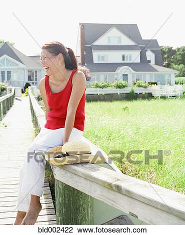 Young woman laughing while sitting on railing View Large Photo Image Stock Image - Young woman laughing while sitting on railing. Fotosearch