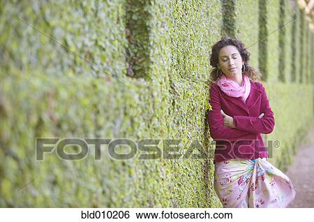 Stock Photograph - Young woman leaning against a hedge. Fotosearch