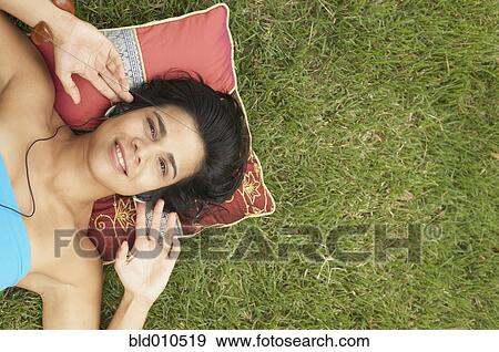 Stock Photo - Young woman lying outside listening to music. Fotosearch