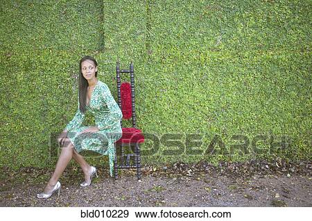 Young woman sitting in front of hedge View Large Photo Image Stock Photo - Young woman sitting in front of hedge. Fotosearch