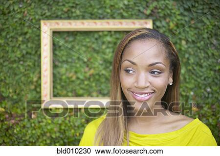 Young woman smiling in front of hedge View Large Photo Image Stock Image - Young woman smiling in front of hedge. Fotosearch