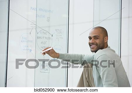 Stock Image - African businessman writing on clear dry erase board. Fotosearch