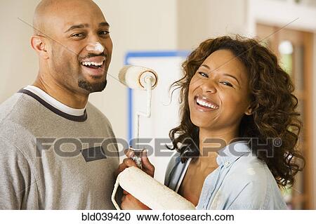 Stock Image - African couple being silly with paint rollers. Fotosearch