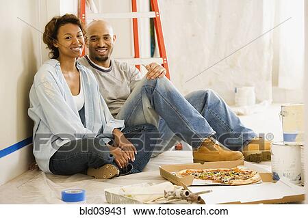 Stock Image - African couple taking lunch break from painting. Fotosearch
