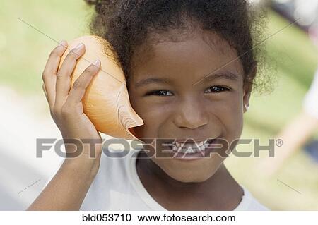 Stock Image - African girl listening to seashell. Fotosearch