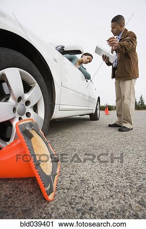 Stock Image - African teenager running over traffic cone at drivers test. Fotosearch